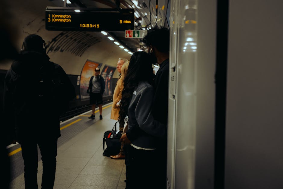 Inside a London underground station, there is a curved tunnel wall with large advertisement posters positioned along the side. The posters include a mix of images and text, such as one promoting a TV
