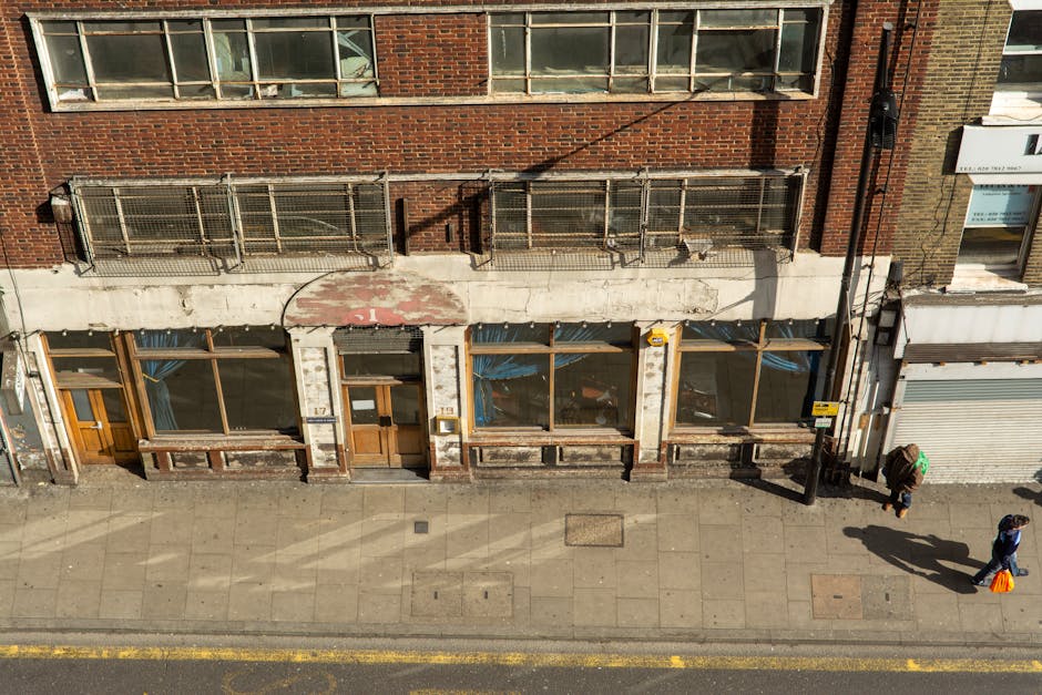 A black wheeled waste collection bin labeled 'COMMERCIAL WASTE ONLY' is positioned in front of a closed storefront with a red-brown wooden exterior and large glass windows, suggesting an interior shop